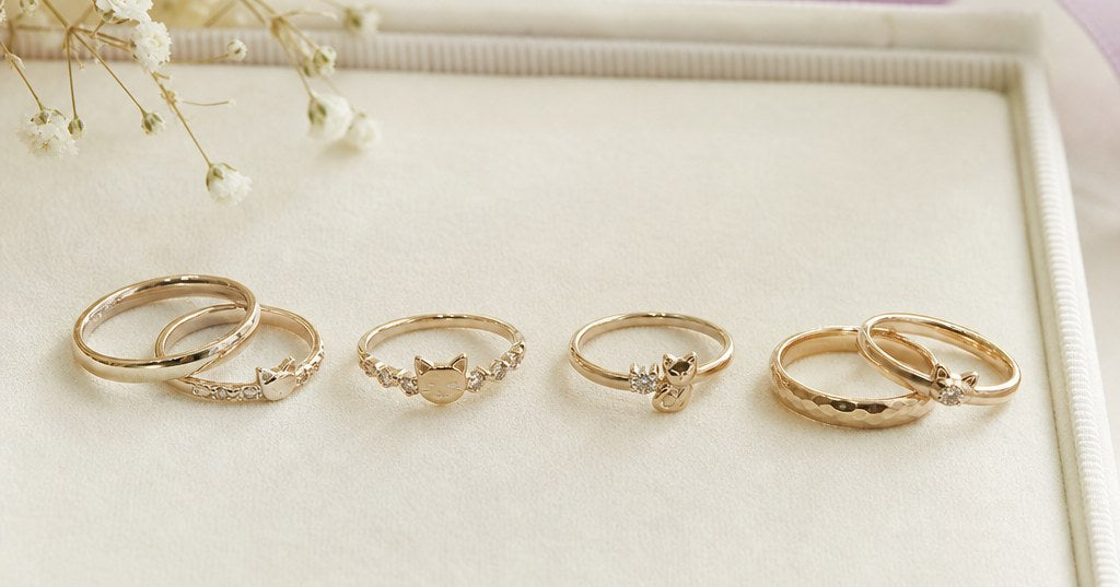 シャンパンゴールドの結婚指輪と繊細な猫モチーフのジュエリーを、アイボリーの背景に上品に並べた比較イメージ